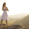 Young woman standing in meditation on the top of a hill