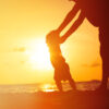 Silhouette of father and little daughter learning to walk at sunset beach